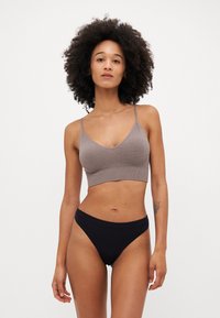 Hnedý ryhovaný crop top s tenkými ramienkami, v kombinácii s hladkými čiernymi vysokými nohavičkami. Jednoduchý dizajn, bez viditeľných vzorov alebo kovania.