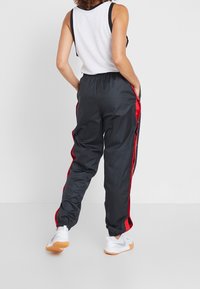 Czarne spodnie sportowe z czerwonymi paskami po bokach, elastycznym pasem i ściągaczami. Noszone z białym topem bez rękawów i białymi trampkami.