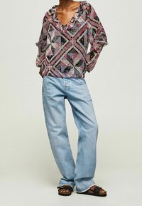 Mönstrad blus i svart, rosa och vitt med volang vid halsen; kombinerad med ljusblå, vida jeanbyxor och svarta sandaler.