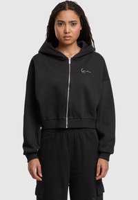 Felpa nera con zip frontale, cappuccio ampio e ricamo del logo bianco. Realizzata in materiale soffice, con maniche lunghe e polsini a coste.