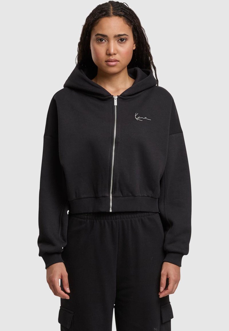 Felpa nera con zip frontale, cappuccio ampio e ricamo del logo bianco. Realizzata in materiale soffice, con maniche lunghe e polsini a coste.