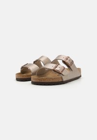 Sandale cu talpă din pluta maro, dotate cu două curele metalice de culoare bej și catarame ajustabile, având o suprafață texturată și un design cu vârful deschis.