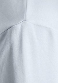Tela de algodón gris claro que muestra una textura suave, con costuras visibles y un brillo sutil. El diseño presenta una silueta simple y limpia.