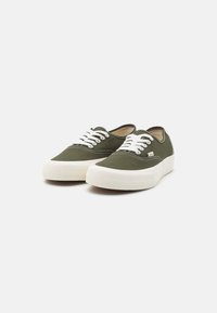 Zapatillas de lona verde oliva con cordones blancos, suelas de goma y detalles de costura en contraste. Diseño de punta redondeada con un estilo de perfil bajo.