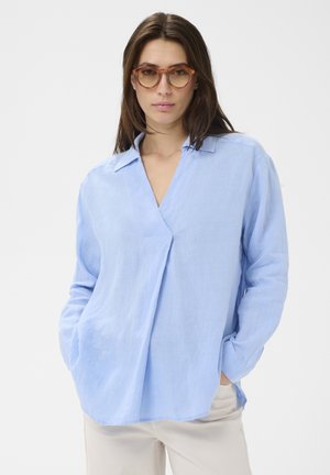 Hellblaues, langärmliges Leinenhemd mit V-Ausschnitt und Kragen. Es hat eine lockere Passform und seitliche Taschen sowie eine glatte Textur.