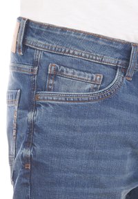 Jeansy dżinsowe w średnim niebieskim kolorze o dopasowanym kroju, z pomarańczowymi przeszyciami, wieloma kieszeniami oraz skórzaną naszywką na pasku.