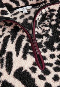 Miękka polarowa kurtka z czarnym i jasnoróżowym nadrukiem w cętki, z przodu zamek błyskawiczny z bordową lamówką oraz biała metka z rozmiarem wewnątrz kołnierza.