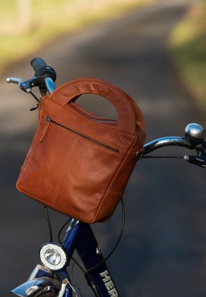 Ruskean nahkalaukku, jossa on pyöreä kahva, etupuolella vetoketjullinen tasku, sileä pinta ja vähäiset saumat, asetettuna polkupyörän ohjaustangolle.