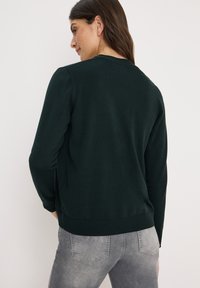 Donkergroen pullover trui met lange mouwen en een ronde halslijn. Zachte, gestructureerde breivoering. Ribgebreide zoom bij de taille en manchetten.