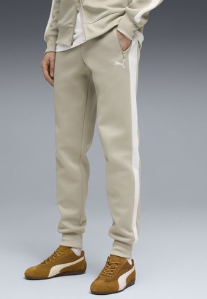 Beige træningsbukser med hvide sidestreger båret med brune Puma-sneakers og en delvist synlig beige lynlåstrøje.