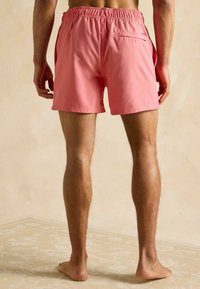 Ružové plavky s elastickým pásom, bočnými vreckami a detailom na zadnom vrecku. Hladký, ľahký materiál, dĺžka nad kolená.