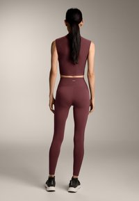 Top corto color vinaccia a coste e leggings coordinati a vita alta. Tessuto morbido, design aderente e dettaglio di branding minimale sulla fascia in vita.