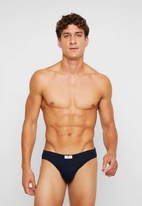 Chiloți bikini de culoare albastru marin, confecționați dintr-un material moale, cu talie joasă și o etichetă mică pe talie. Textură netedă și acoperire minimă.