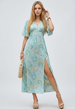 Mujer con un vestido maxi de patrón azul claro con mangas hasta el codo y una abertura lateral, sosteniendo un bolso tejido, y llevando sandalias plataforma beige.
