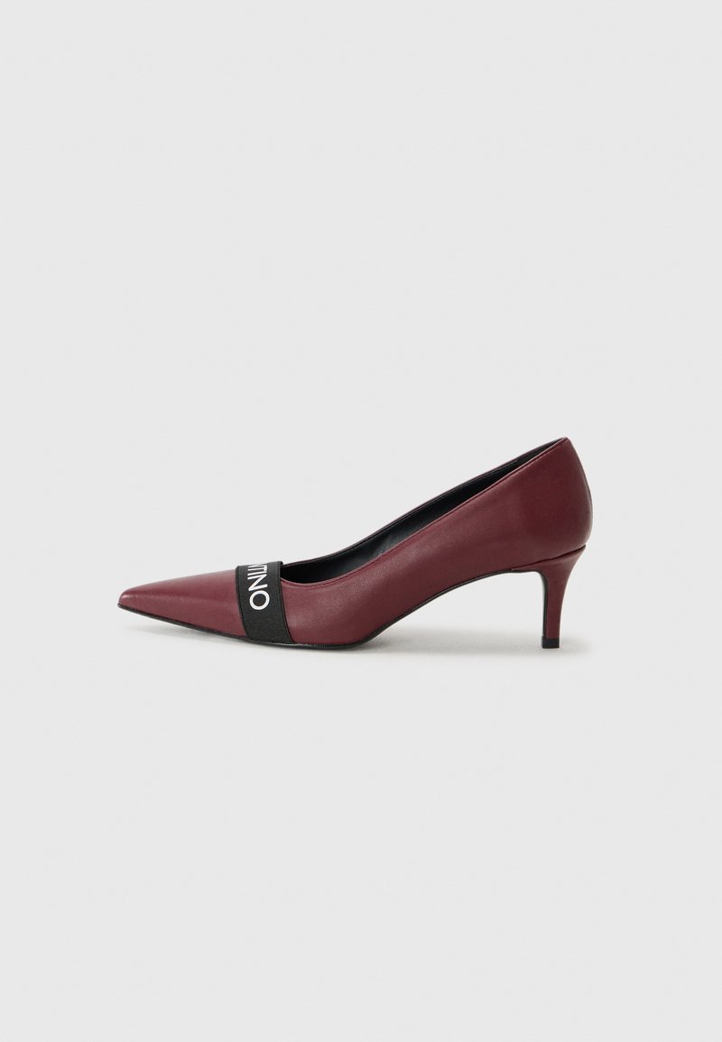 Scarpa con tacco alto in pelle borgogna, con punta affilata e una fascia nera con testo bianco che attraversa il piede. Tacco stiletto sottile.