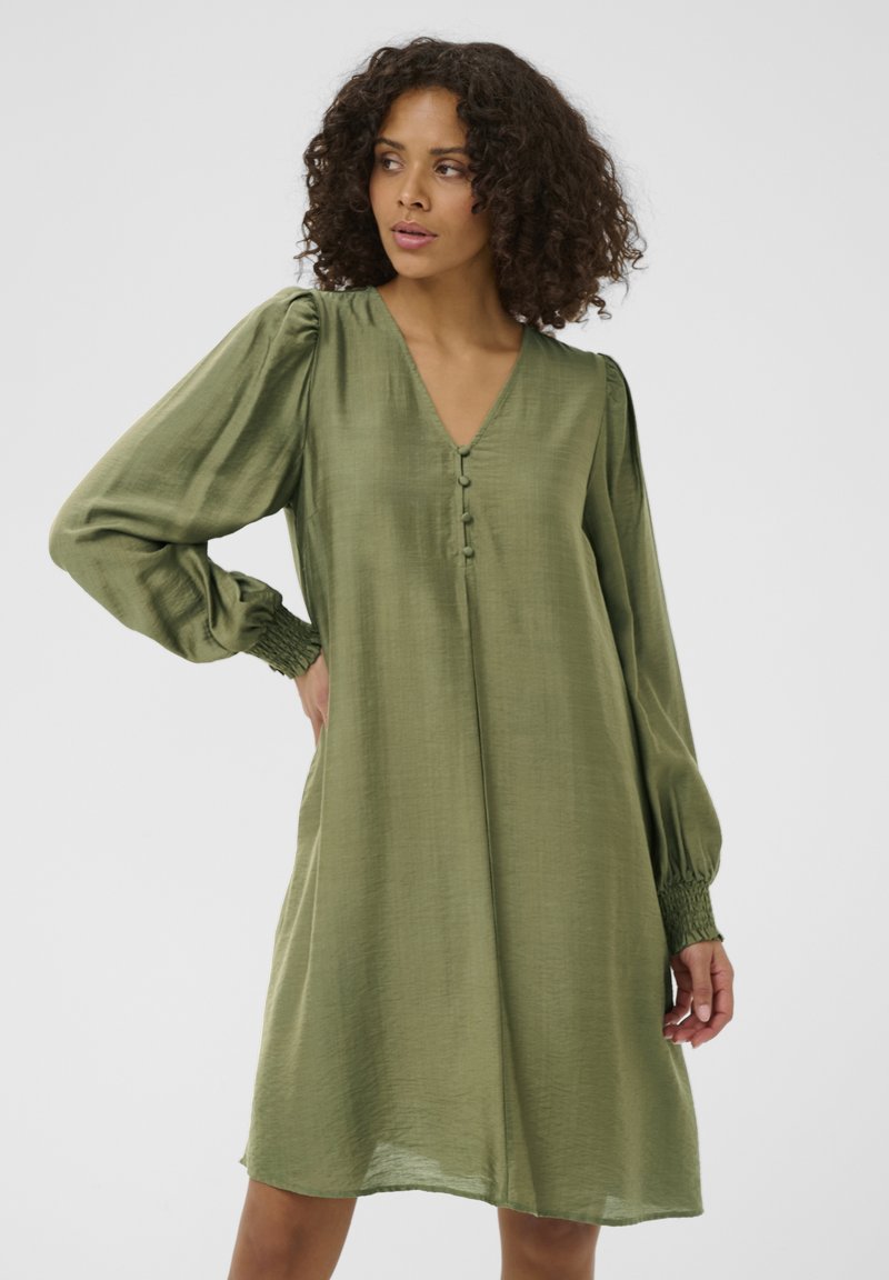 Robe mi-longue couleur vert olive avec un décolleté en V, dotée d'un devant boutonné et de manches longues bouffantes avec des poignets smockés. Texture lisse.