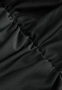 Gros plan sur un tissu côtelé noir avec des coutures élastiques froncées créant des plis texturés.