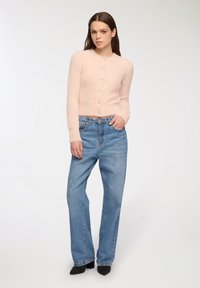 Cardigan fluffy di colore rosa chiaro, con bottoni sulla parte anteriore, abbinato a jeans blu a vita alta e scarpe nere con punta. Tessuto liscio, design aderente.