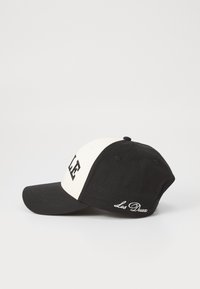Fekete-fehér baseball sapka strukturált koronával, ívelt karimával, hímzett betűkkel elöl, és "Les Deux" felirattal az oldalon.
