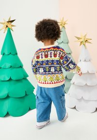 Maglione lavorato a maglia colorato con motivi natalizi, colletto crema e orlo a coste, abbinato a un denim blu largo e scarpe da ginnastica bianche.