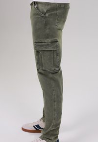 Olive green cargo pants with a slim fit, featuring a large side pocket and subtle fading. Paired with white sneakers.