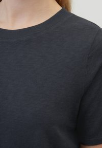 T-shirt en coton gris foncé avec un col rond côtelé. Manches courtes et texture lisse, vue du cou jusqu'à la zone des épaules.