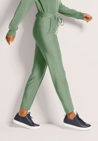 Helblau groene joggers met een trekkoord in de taille, zijzakken en een taps toelopende pasvorm, gecombineerd met marineblauwe sneakers met witte zolen.