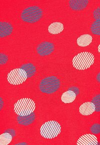 Roter Stoff mit verschieden großen Kreisen in Blau, Weiß und Creme. Die Kreise weisen durchgehende und gestreifte Muster auf, was ein texturiertes Erscheinungsbild erzeugt.