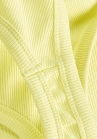 Gul ribbad tyg har en mjuk textur, vertikala linjer och kontrasterande sömmar. Materialet verkar lätt och flexibelt.