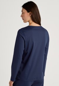 Navy long-sleeve shirt with a round neckline, smooth texture, and a relaxed fit, viewed from the back, featuring minimal detailing.