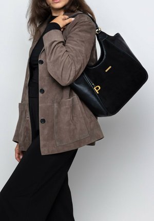 Black leather handbag with suede accents, gold hardware, and a curved shape, carried with a brown suede jacket featuring large pockets.