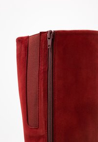 Czerwone zamszowe botki z bocznym zamkiem błyskawicznym i elastycznym panelem. Charakteryzują się gładką teksturą i wysokim fasonem, odpowiednie do różnych stylizacji.