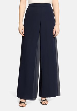 Pantalon large marine avec un pli fendu devant, porté avec des sandales noires à lanières et un haut blanc rentré.