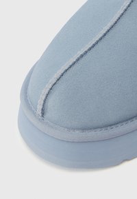Gros plan de l'orteil arrondi d'une chaussure en daim bleu clair avec des coutures détaillées et un bord de semelle texturé.