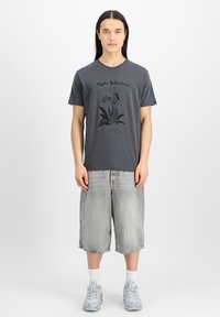 Grå bomulls T-shirt med en svart grafisk design av en kvinna och text. Kombinationen med ljusgrå denimshorts och mönstrade grå sneakers.