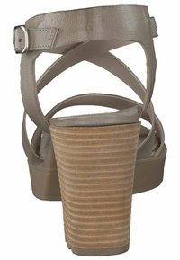 Sandali con tacco alto beige con fasce incrociate in pelle, una suola in legno texturizzato e una finitura liscia sulla parte superiore.