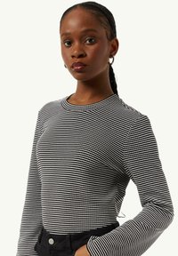 Long-sleeve top in black and white striped material, features a round neckline and fitted design. Worn with black high-waist pants.