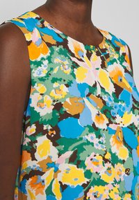 Top sin mangas con estampado floral que presenta una mezcla de colores vibrantes: azul, naranja, amarillo y verde, confeccionado en una tela ligera con una textura suave y cuello redondo.
