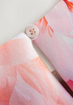 Textilie s světle růžovou látkou s květinovým vzorem a kulatým, hladkým knoflíkem na průsečíku, se světle hněvým šitím.