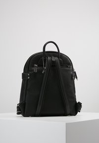 Sac à dos noir en cuir texturé, avec un sommet arrondi, des bretelles réglables doubles, une poche zippée à l'avant et un petit détail de porte-clés.