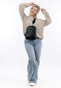 Black leather crossbody bag with a rounded shape, textured finish, and adjustable strap. Model wears a beige sweater and light blue jeans.