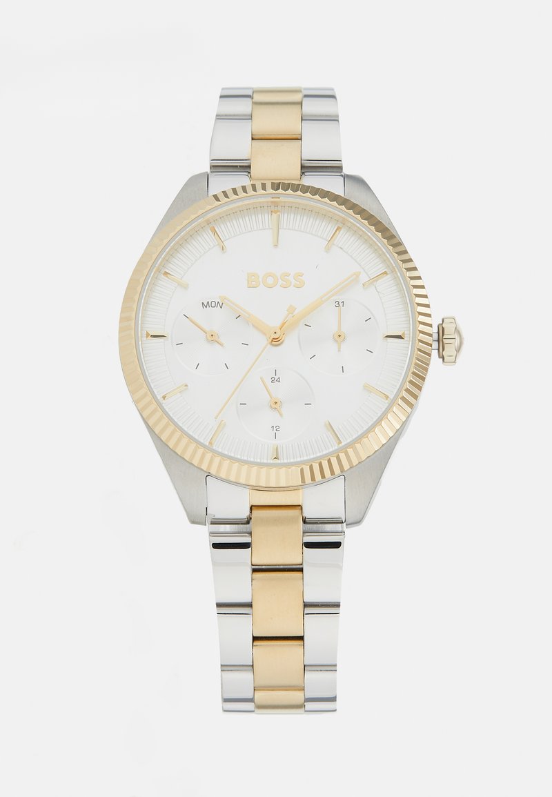 Reloj de pulsera en tonos plateado y dorado con un dial blanco, marcadores de hora negros, pantalla de fecha y una pulsera de acero inoxidable con eslabones alternos.