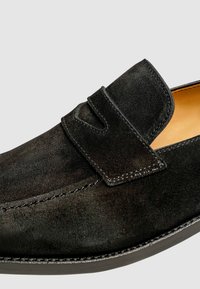 Schwarzer Wildleder Slipper mit glatter Textur, kontrastierenden Nähten und einer abgerundeten Zehenpartie. Mit einem Riemen über der Oberseite.