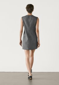 Robe sans manches grise avec une silhouette ajustée, tissu texturé et détails de couture dans le dos, assortie à des chaussures noires à lacets.