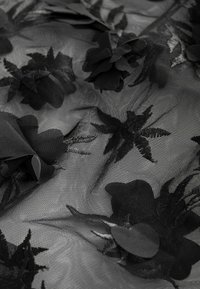 Zwarte tule stof met textuurpatronen van bloemen en bladeren, met gelaagde bloemen en bladeren in verschillende vormen en groottes.