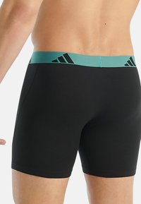 Czarne sportowe spodenki z turkusowym paskiem w talii ozdobionym trzema czarnymi paskami. Wykonane z elastycznego materiału, zaprojektowane dla komfortu i wsparcia.