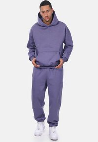 Lila Sweatshirt- und Hosen-Set aus weichem Stoff. Verfügt über eine Fronttasche, eine lockere Passform, gerippte Bündchen und weiße Sneakers.