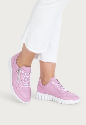 Person wearing light pink sneakers with white soles and white laces, paired with white cropped pants with frayed hems.