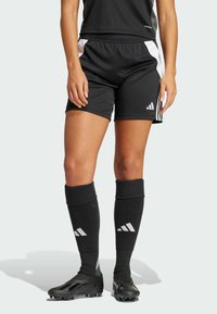Shorts atletici negri cu accente albe pe laterale, asortați cu ciorapi negri până la genunchi, ce au un logo. Pantofii sunt negri, cu un design elegant și texturat.