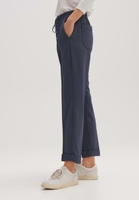 Marina, löst sittande byxor i strukturerad tyg med elastisk midja, dragsko och sidofickor, kombinerat med vita sneakers.